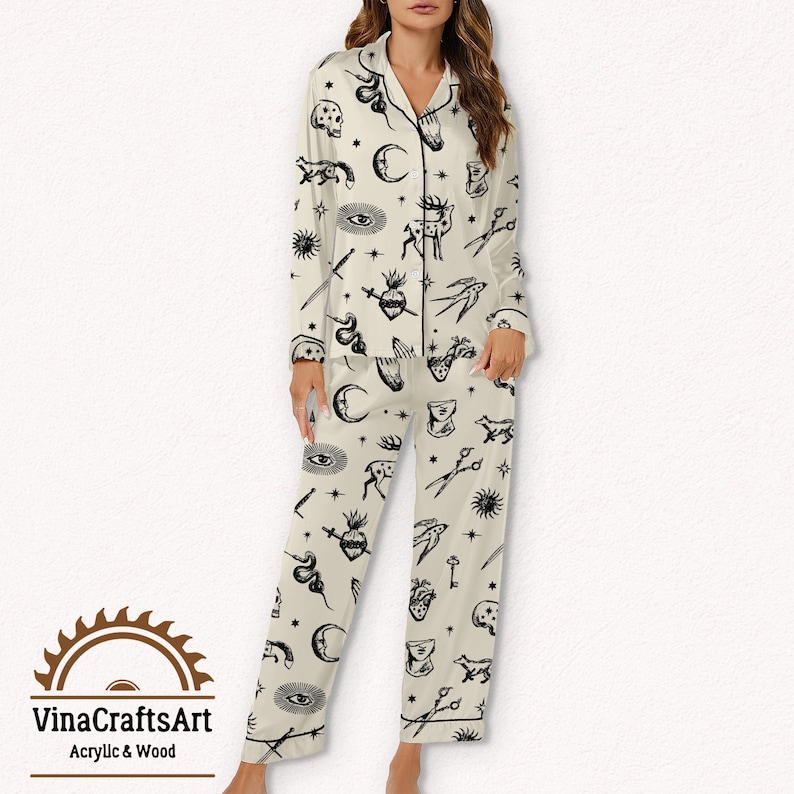 Pode incluir: Conjunto de pijama creme com um padr&atilde;o preto com tema oculto. A parte superior de manga comprida e as cal&ccedil;as apresentam v&aacute;rios s&iacute;mbolos como luas, olhos, cora&ccedil;&otilde;es e tesouras. O conjunto tem acabamentos pretos e uma parte superior abotoada.