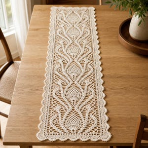 May include: A long, rectangular off-white crochet table runner featuring an intricate, repeating pineapple-inspired lace pattern. The runner has a scalloped edge design and is crafted with fine thread, displaying a delicate, openwork texture.