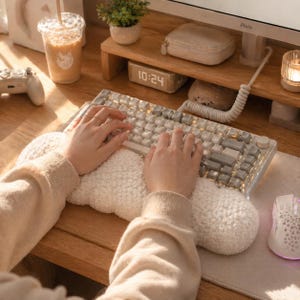 May include: A person typing on a white and gray mechanical keyboard with a fluffy white wrist rest. The keyboard is on a wooden desk, with a computer monitor, mouse, and a drink in the background. The time on the digital clock is 10:24.