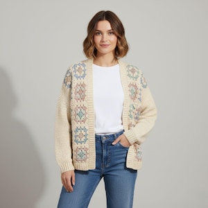 May include: Cream-coloured open cardigan with a geometric pattern in pastel shades. The sweater features long sleeves and a relaxed fit. The model is wearing a white t-shirt and blue jeans.