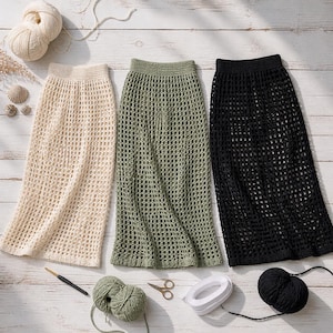 May include: Three crochet skirts in cream, olive green, and black are displayed on a light wood surface. The skirts have a netted design. Yarn balls, a crochet hook, scissors, and other craft supplies are arranged around the skirts.