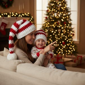 Könnte beinhalten: Mutter und Kind tragen passende rot-weiß gestreifte Weihnachtsmützen. Das Kind trägt einen rot-weißen Strampler. Im Hintergrund ist ein Weihnachtsbaum mit Lichtern zu sehen. Die Mutter zeigt mit dem Finger.