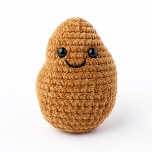 May include: A plush, brown crocheted potato with a smiling face. The toy has black safety eyes and a stitched black mouth. The potato is made of a soft, textured yarn and is designed to look like a friendly character.