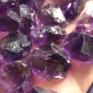 May include: A collection of raw amethyst crystals in various sizes and shapes. The crystals are a deep purple colour and have a natural, rough texture.