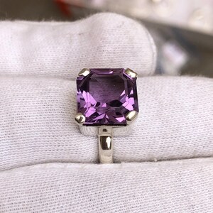 Puede incluir: Un anillo de plata con una gran amatista de talla cuadrada. El anillo tiene un estilo simple y elegante.
