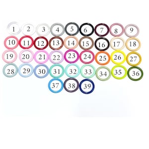 Op de afbeelding: Een verzameling van 39 kleurrijke ronde ringen, elk met een unieke tint en een nummer van 1 tot 39. De ringen zijn gerangschikt in rijen en kolommen, met een breed scala aan kleuren, van helder tot zwart, inclusief tinten roze, blauw en groen.