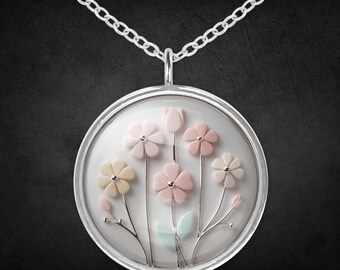 May include: A silver necklace with a circular pendant displaying a floral arrangement. The pendant features a white backdrop with pink, yellow, and pale blue flowers. The necklace has a fine chain.