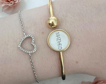 Op de afbeelding: Drie armbanden: een zilveren kettingarmband met een hartvormige bedel en twee goudkleurige armbanden. Eén gouden armband heeft een ronde bedel met de naam "MATHEO" erop gedrukt. De andere gouden armband heeft een kogelvormige bedel.