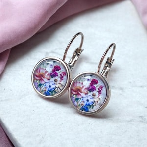 Könnte beinhalten: Ein Paar silberne Creolen mit einem Blumenmuster. Die Ohrringe haben einen runden Glascabochon mit einem bunten Blumenmuster.