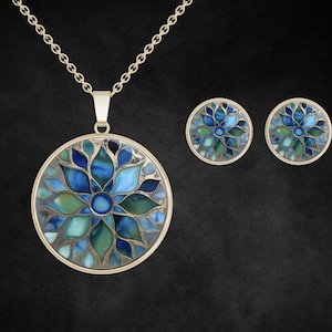 May include: A gold-coloured pendant necklace and matching stud earrings set. The pendant and earrings feature a circular design with a blue and green floral pattern. The jewellery set is displayed on a black background.