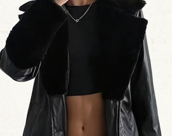 May include: A black faux leather jacket with a faux fur collar and cuffs. The jacket has a classic design with a wide lapel and a tailored fit. The model is wearing blue jeans and a black top.