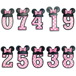 May include: A collection of ten number cutouts, each featuring a black mouse ear design with a pink bow. The numbers are pink with white polka dots. The numbers are 0, 7, 4, 1, 9, 2, 5, 6, 3, and 8.