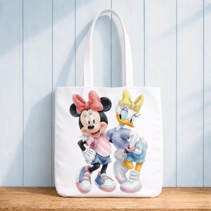 Op de afbeelding: Een witte draagtas met een kleurrijke afbeelding van Minnie Mouse en Katrien Duck die naast elkaar staan. Minnie draagt een roze strik en shirt met een blauwe korte broek, terwijl Katrien een gele strik en blauw shirt met blauwe korte broek draagt.