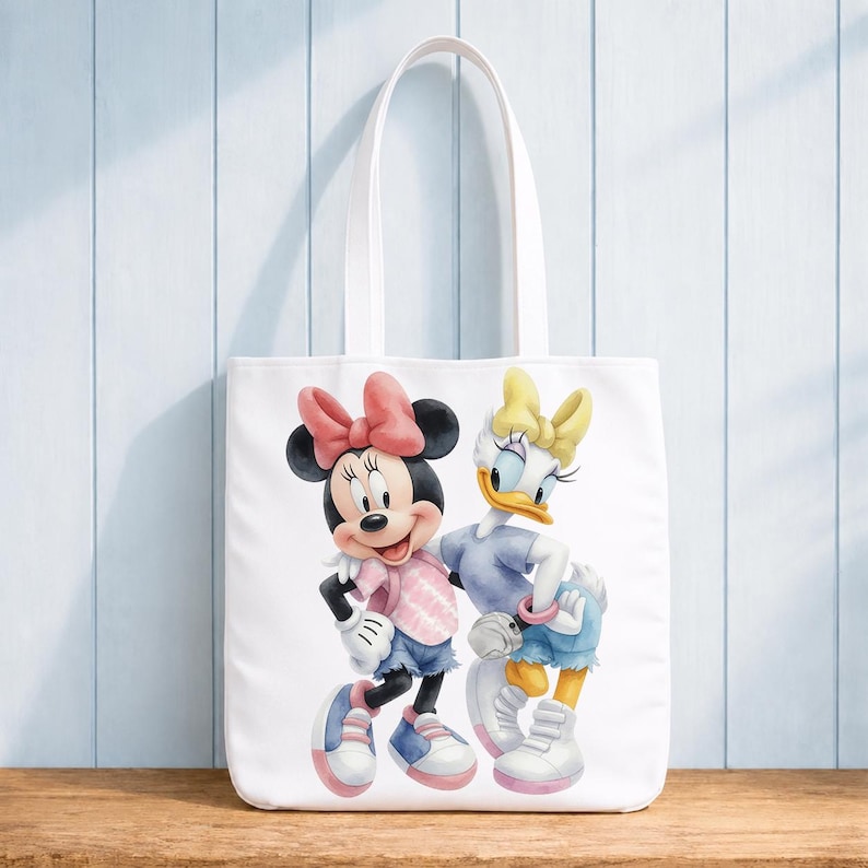 Op de afbeelding: Een witte draagtas met een kleurrijke afbeelding van Minnie Mouse en Katrien Duck die naast elkaar staan. Minnie draagt een roze strik en shirt met een blauwe korte broek, terwijl Katrien een gele strik en blauw shirt met blauwe korte broek draagt.