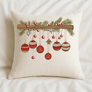 Christmas ornament embroidery design on cream pillow – red baubles and pine branch stitched holiday décor on cozy white bedding