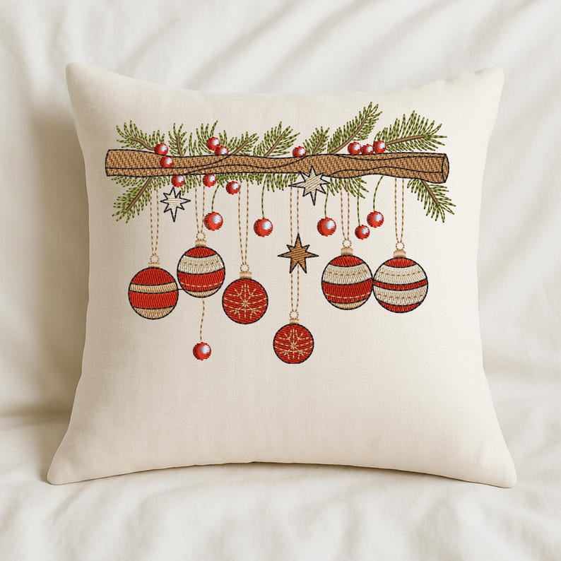 Christmas ornament embroidery design on cream pillow – red baubles and pine branch stitched holiday décor on cozy white bedding