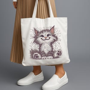 White tote bag featuring fluffy cat embroidery design, styled with pleated skirt and sneakers, perfect for pet lovers and machine embroidery fans.