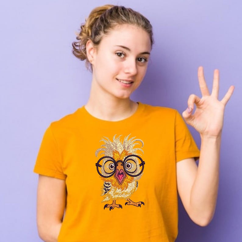 Smiling girl wearing bright yellow t-shirt with cute owl embroidery design featuring large glasses, shown on purple background – perfect for fun American embroidery projects.