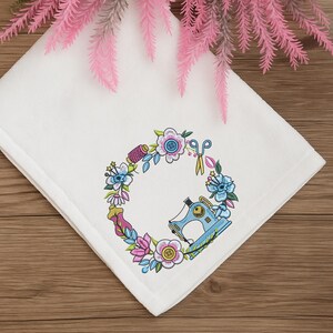 Sewing machine floral embroidery frame stitched on a white towel. Displayed on wood with pink floral accents. Ideal for custom gifts and embroidery decor