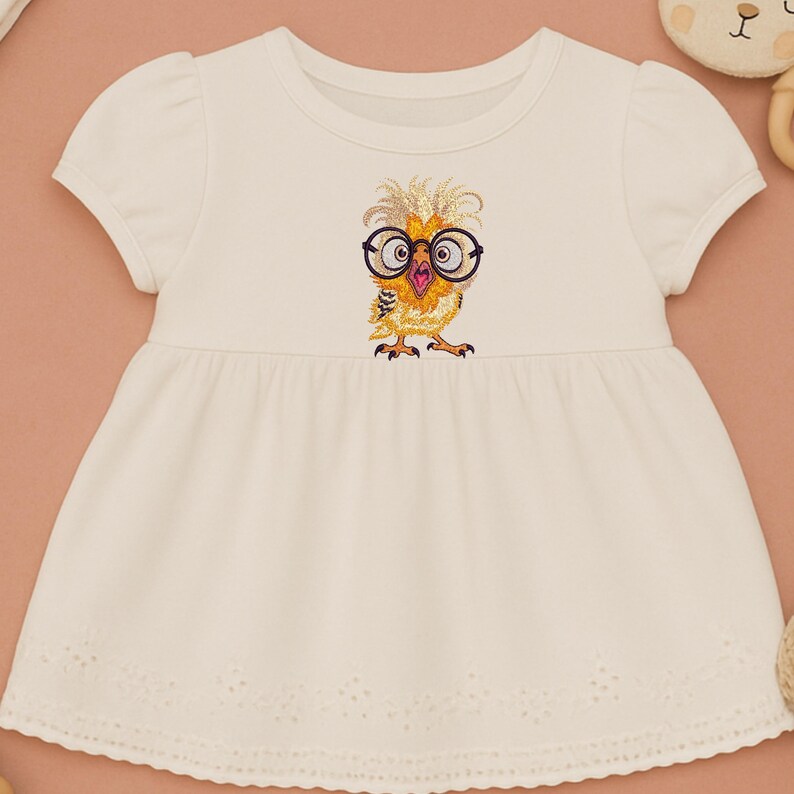 White baby dress with cute owl embroidery design featuring glasses, flat lay styled with neutral soft toys on peach background – perfect for baby shower gifts and newborn outfits in USA and Europe.
