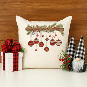 Christmas ornament embroidery design on white pillow – festive red baubles and pine branch with holiday décor and gift box
