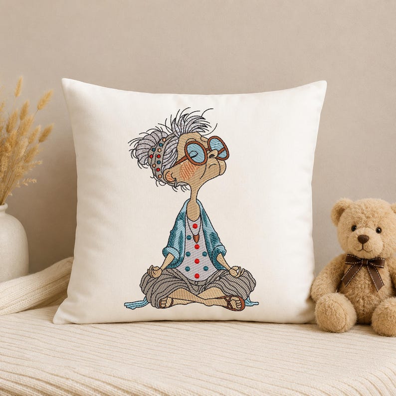 White decorative pillow featuring a Meditating Grandma machine embroidery design with a funny zen yoga granny, showing the finished embroidery for home décor and cushion projects