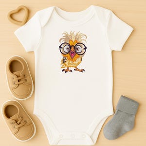 Flat lay of cream baby onesie with cute owl embroidery featuring glasses, surrounded by tan baby shoes, heart-shaped teether, and gray sock – ideal for newborn gifts or nursery decor in USA and Europe.