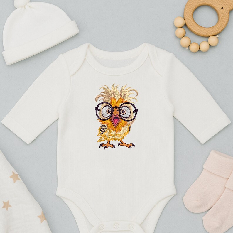 White baby onesie featuring cute baby owl embroidery design with glasses, styled flat lay with baby socks, hat, and wooden teether – ideal for newborn gifts in USA and Europe.