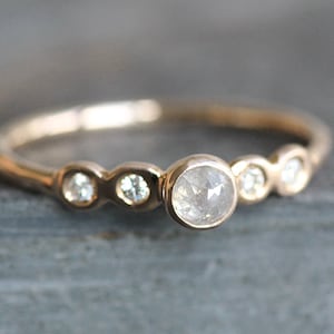 May include: A delicate gold ring with a single large round diamond and smaller diamonds on either side. The ring is set in a simple band.