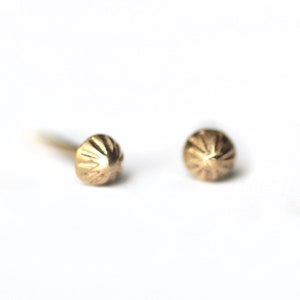 May include: A pair of gold stud earrings with a textured, dome-shaped design.
