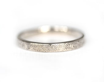 May include: A silver band ring with an intricate floral design engraved around the entire band.