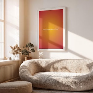 May include: A framed art print with a gradient of red, orange, and yellow. The print has the text "better an oops than a what if" in a white, elegant font. The print is hanging above a beige, curved sofa.