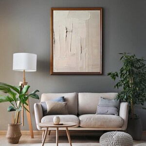 Può includere: Un salotto con un divano beige, cuscini, un tavolino in legno e una lampada da terra con paralume bianco. Un dipinto astratto con cornice in legno è appeso alla parete. Le piante in vaso aggiungono un tocco naturale.