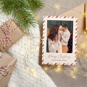 May include: A Christmas card with a family photo, framed with red and green diagonal stripes. The card reads "Merry Christmas" in gold script, with gifts wrapped in brown paper and string.