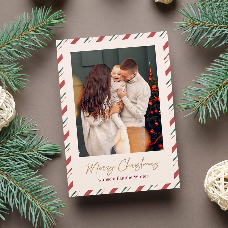 May include: A Christmas card featuring a family portrait with a festive border. The card has a cream background with a red and green striped border. The text "Merry Christmas" is written in gold script, with additional text below. The card is surrounded by pine branches and decorative balls.