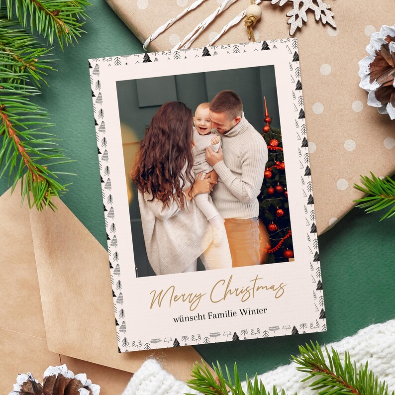 May include: A Christmas card featuring a family portrait. The card has a cream-colored border with black and white tree designs. The text "Merry Christmas" is written in gold script, with additional text below. The background includes a Christmas tree and wrapped gifts.