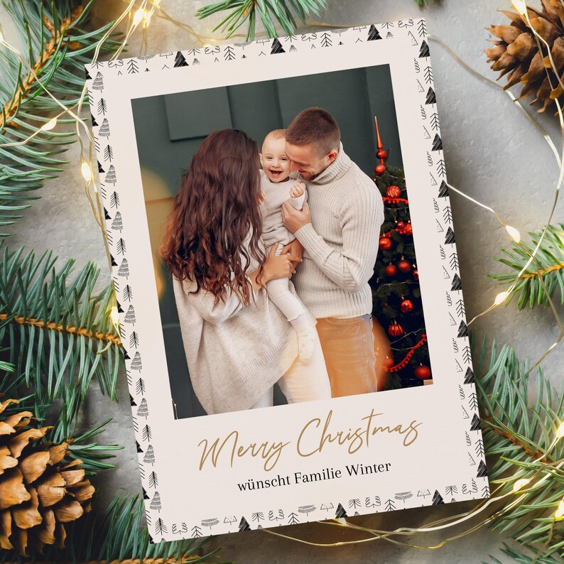 May include: A Christmas card with a family photo inside a white frame. The frame is decorated with black and white tree designs. The words "Merry Christmas" are written in gold script, with the German phrase "w&uuml;nscht Familie Winter" below.
