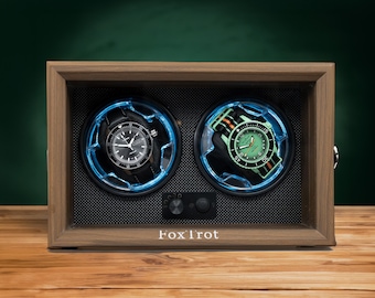 May include: A wooden watch winder with two watch compartments, each illuminated with blue light. The winder displays two watches, one with a black face and the other with a green face. The text "Fox1rot" is visible on the front.