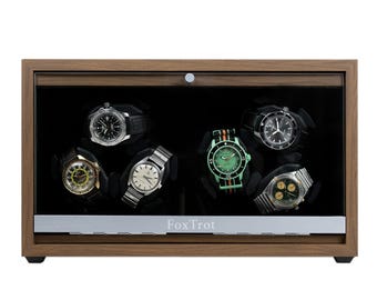 May include: A rectangular wooden watch winder box with a glass front door and a silver-toned base featuring the text FoxTrot. Inside, six wristwatches with various dial colours and metal or fabric straps are mounted on black rotating holders.