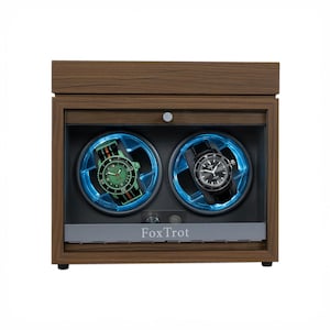 May include: A wooden watch winder with two compartments, each illuminated with blue light and holding a wristwatch. One watch has a green face and striped band, the other a black face and band. The name "FoxTrot" is printed on the front.