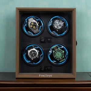 May include: A wooden watch winder with four compartments, each illuminated with blue light. The winder holds four different watches with various band and face designs. The text "FoxTrot" is printed on the bottom.