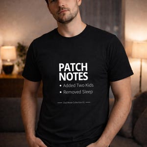 Puede incluir: Camiseta negra con texto blanco: "PATCH NOTES" con los puntos "Added Two Kids" y "Removed Sleep". Debajo, "Dad Mode Collection 01". La persona lleva vaqueros azules.