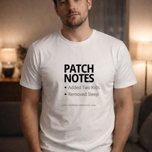Puede incluir: Camiseta blanca con el texto "PATCH NOTES" encima de "Added Two Kids" y "Removed Sleep". La camiseta forma parte de la "Dad Mode Collection 01". El modelo lleva vaqueros azules.