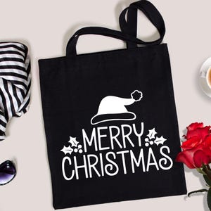 May include: Black tote bag with white text and a Santa hat graphic that reads "MERRY CHRISTMAS". The bag has black handles and is made of a sturdy material. A festive holiday accessory.