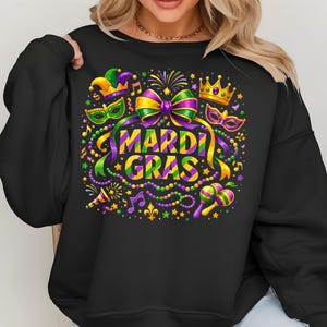 May include: Black sweatshirt with a colorful Mardi Gras design. The graphic includes the words "Mardi Gras" in yellow and purple, along with masks, musical notes, and a crown. The design features green, purple, and gold accents.