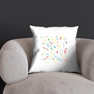 K&ouml;nnte beinhalten: Ein wei&szlig;es Kissen mit einem bunten Konfetti-Design. Das Konfetti besteht aus roten, gelben, blauen und gr&uuml;nen Wellenlinien.