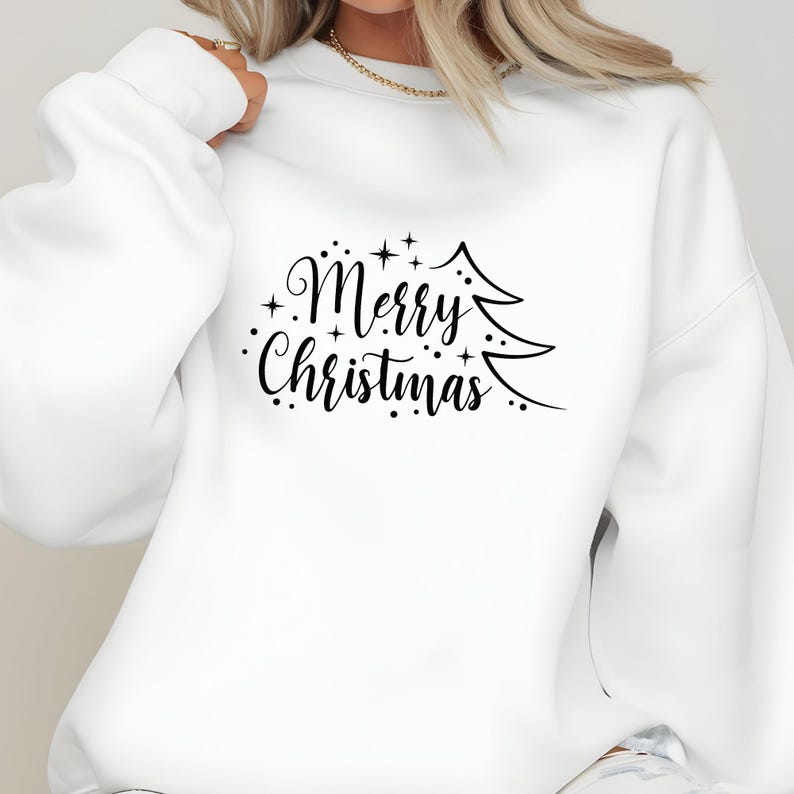 May include: White sweatshirt with the text "Merry Christmas" in a black script font, accompanied by a stylized Christmas tree graphic. The design includes small star accents, creating a festive holiday theme.