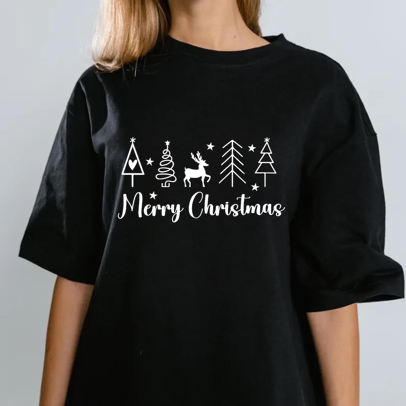 May include: Black t-shirt with a white Christmas design. The design includes a Christmas tree, a deer, stars, and the words "Merry Christmas" in a script font. The shirt has short sleeves.
