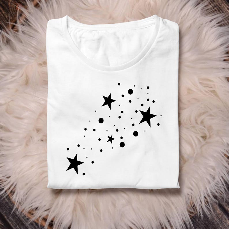 K&ouml;nnte beinhalten: Wei&szlig;es T-Shirt mit einem schwarzen Design aus Sternen und Punkten. Die Sterne sind diagonal angeordnet, mit den Punkten, die um sie herum verstreut sind.