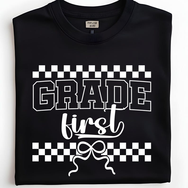 Op de afbeelding: Zwart T-shirt met de witte tekst "GRADE first", omringd door een dambordpatroon. Een witte strik staat onder de tekst. Het T-shirt is opgevouwen.